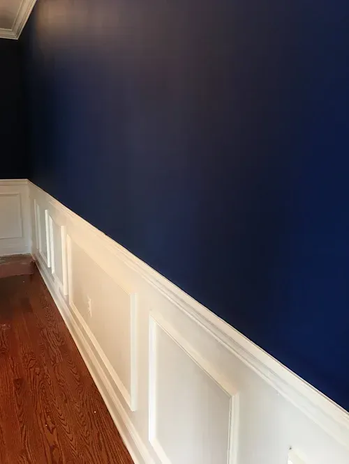 Navy blue wall with white wainscoting and hardwood floor in a room.