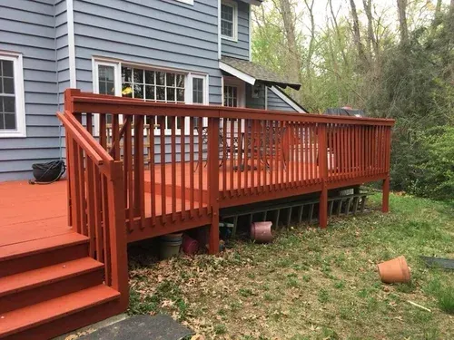 Red painted wooden deck attached to a blue house with steps leading down to a grassy yard.