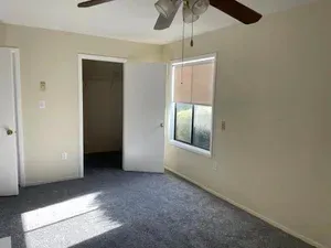 Empty bedroom with gray carpet, beige walls, closet, and a window with blinds.
