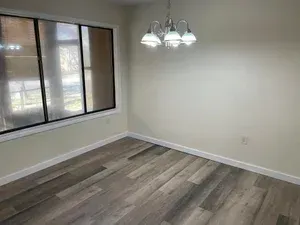 Empty dining room with wood-look floor, window, and chandelier; cream-colored walls and trim.