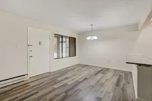 Empty dining area with light wood floor, white walls, and a window.