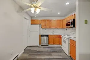 A small kitchen with light brown cabinets, white appliances, and gray flooring.
