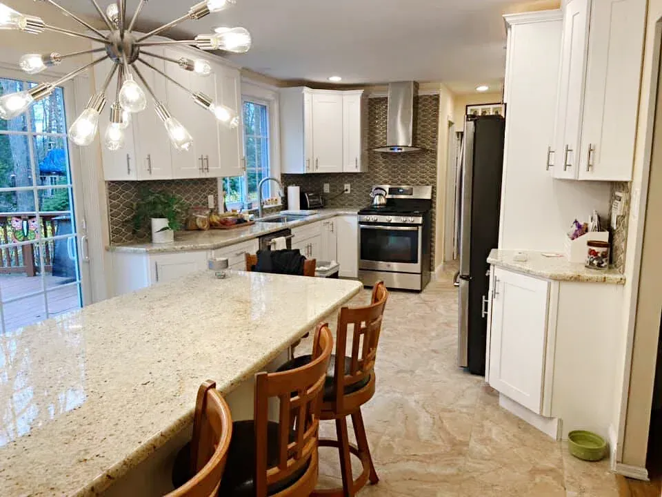 Bright white kitchen with a granite island, stainless steel appliances, and wood bar stools.