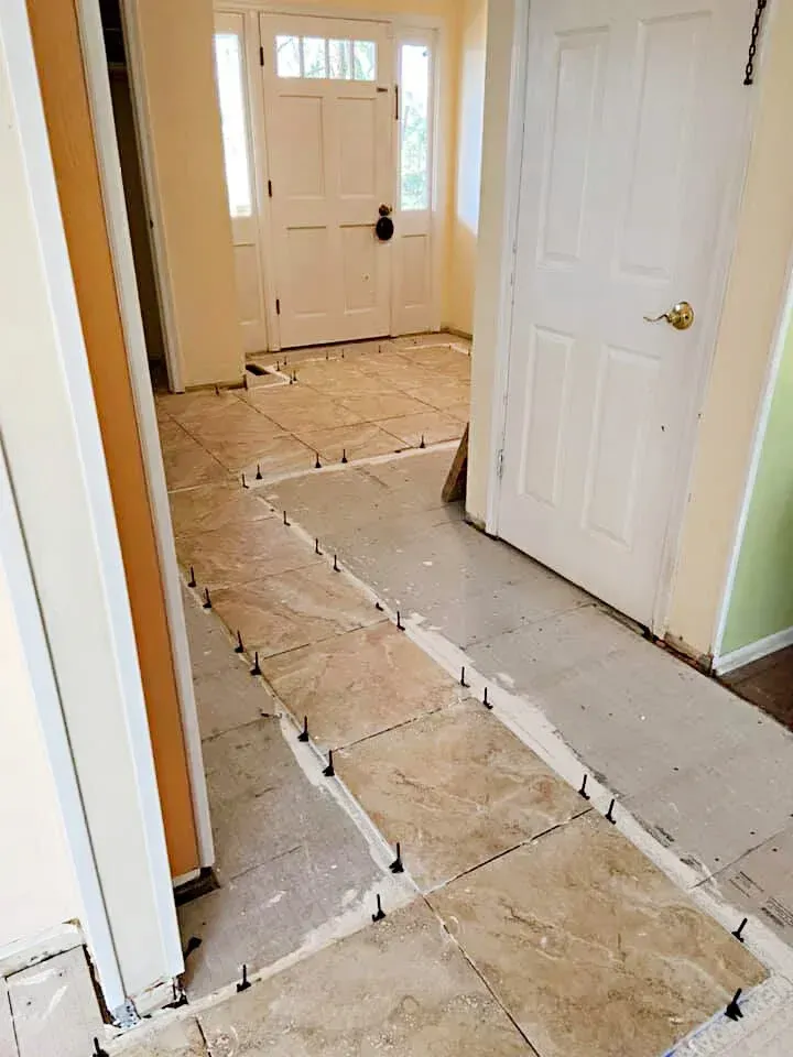 Hallway floor tiling in progress; tan tiles laid with spacers, leading toward a white door.