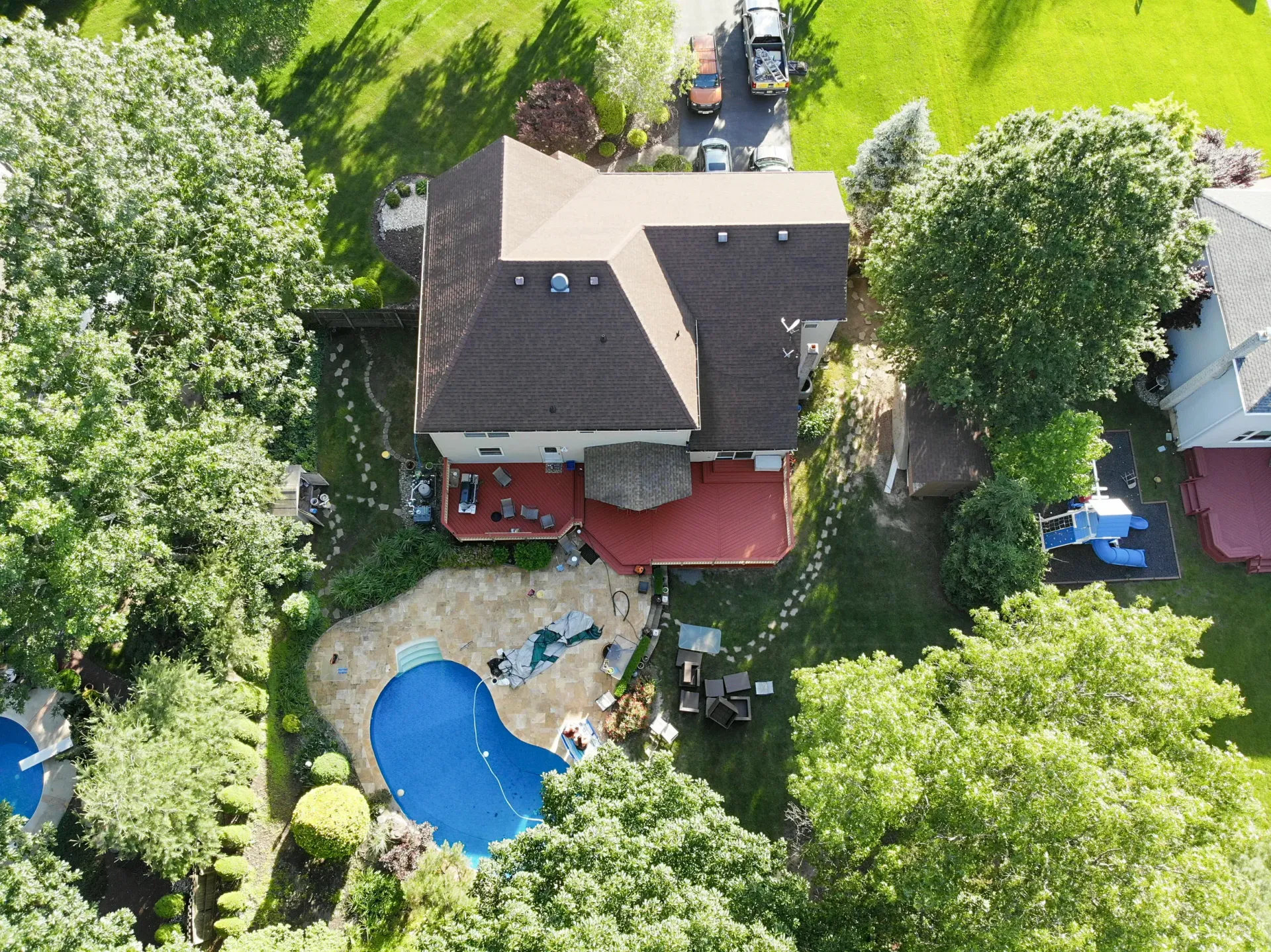 Aerial view of a house with a pool and trees in a residential neighborhood.