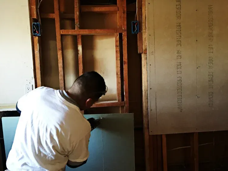 Man installing drywall on a wooden frame wall, interior construction.