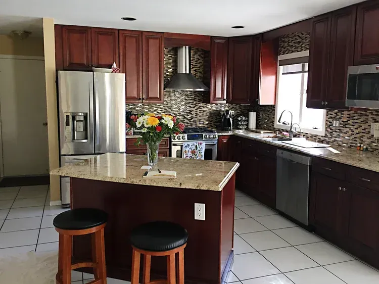 Kitchen with dark wood cabinets, stainless steel appliances, and a granite island with stools.