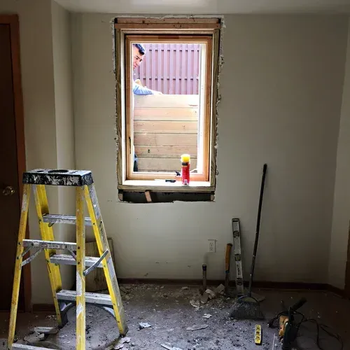 A room under construction with a yellow ladder, open window, and person working outside.