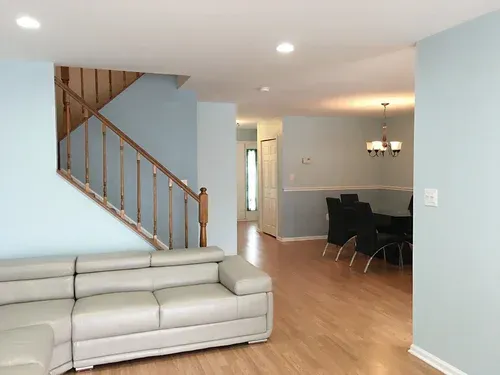 Interior view of a home with light blue walls, wooden stairs, and a dining area with a black table and chairs.