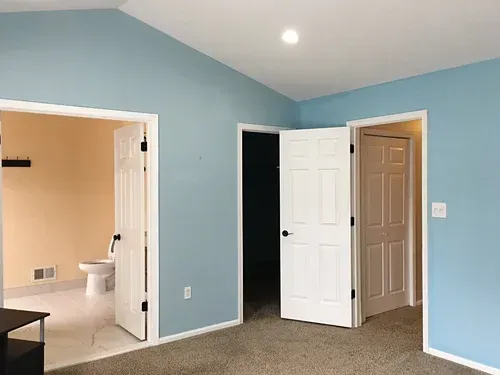 A room with blue walls and three doorways. One doorway leads to a bathroom.
