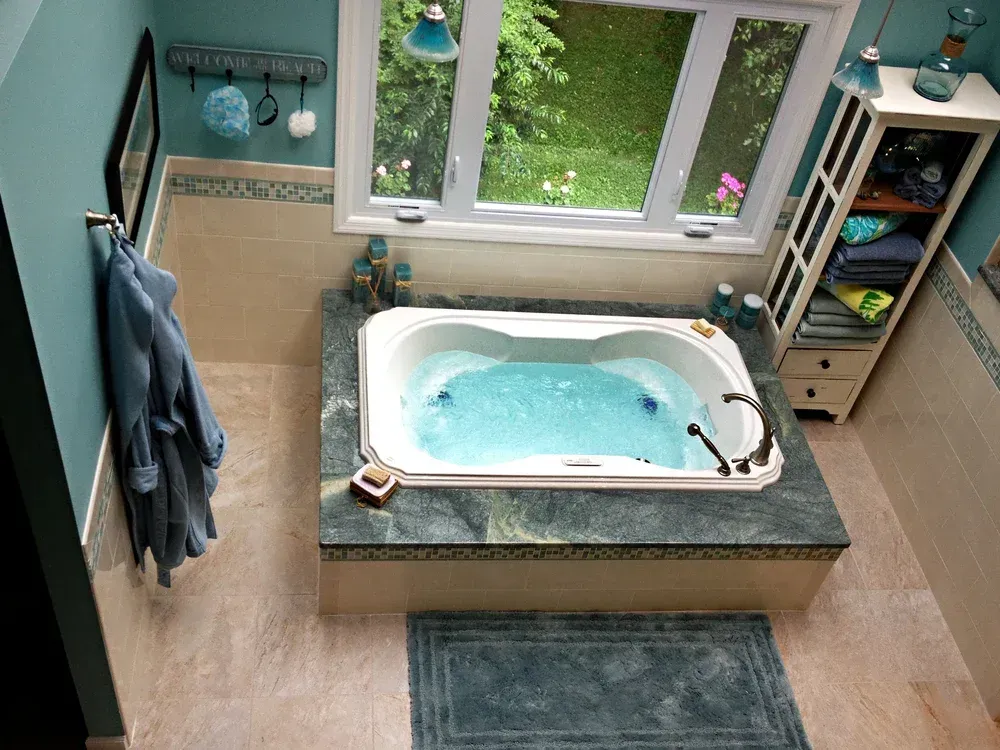 Overhead view of a bathroom with a jacuzzi tub. Blue-green walls, a window, and a white storage cabinet.
