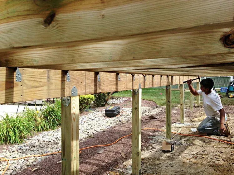 Person building deck, hammering joist brackets.