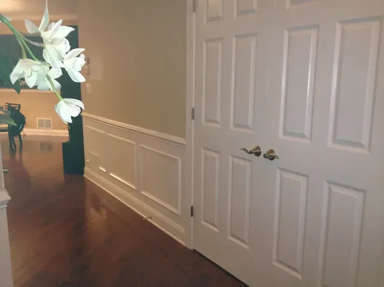 White door with gold handles, white paneling, and wood floor in a hallway.