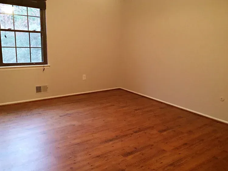 Empty room with a window, tan walls, and wood-look flooring.