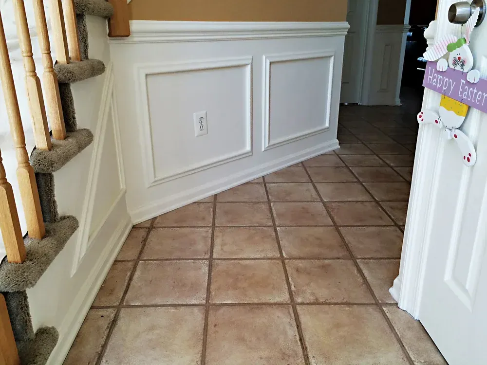 Entryway with tile floor, white wainscoting, and stairs on the left. A door with a Happy Easter sign is on the right.