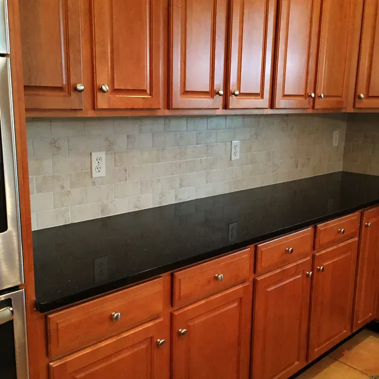 Kitchen with black countertop, light backsplash, and brown wooden cabinets.