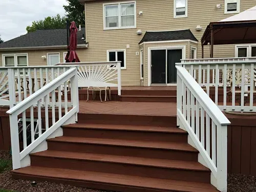 Wooden deck with white railings and stairs leading to a house with a beige exterior.