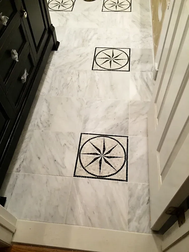 White marble floor with black compass rose tiles. Black cabinet on the left, white door on the right.