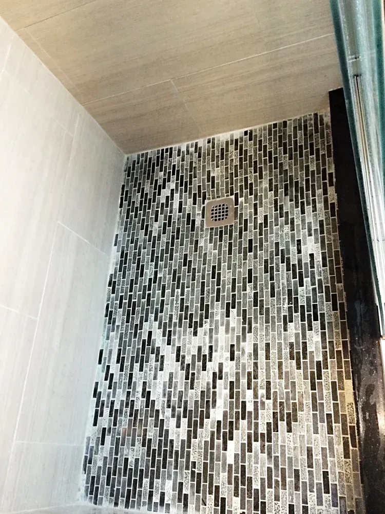 Shower with black, gray, and white mosaic tile accent wall; light gray tile side wall.