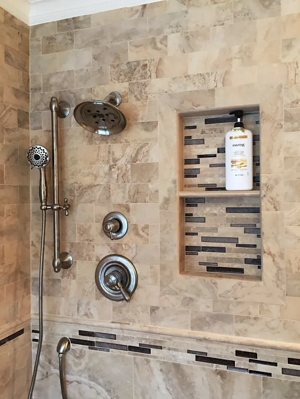 Shower with beige and gray tile, built-in shelf with soap, and chrome fixtures.