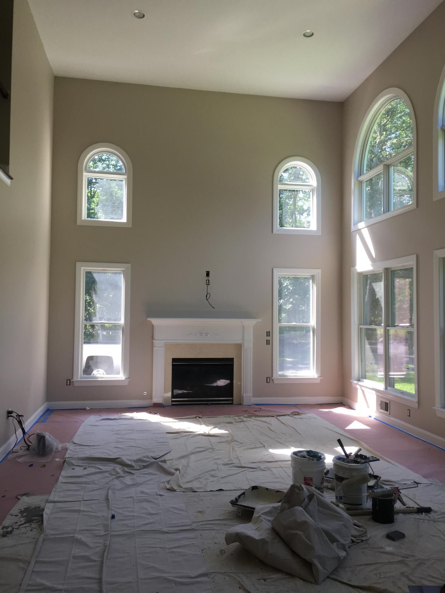 Living room interior with beige walls, fireplace, arched and rectangular windows, painting supplies on the floor.