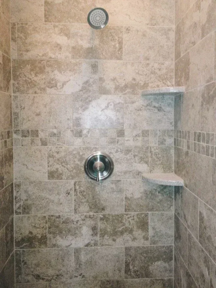 Shower with beige-toned tile, built-in shelves, and a silver shower head and control.