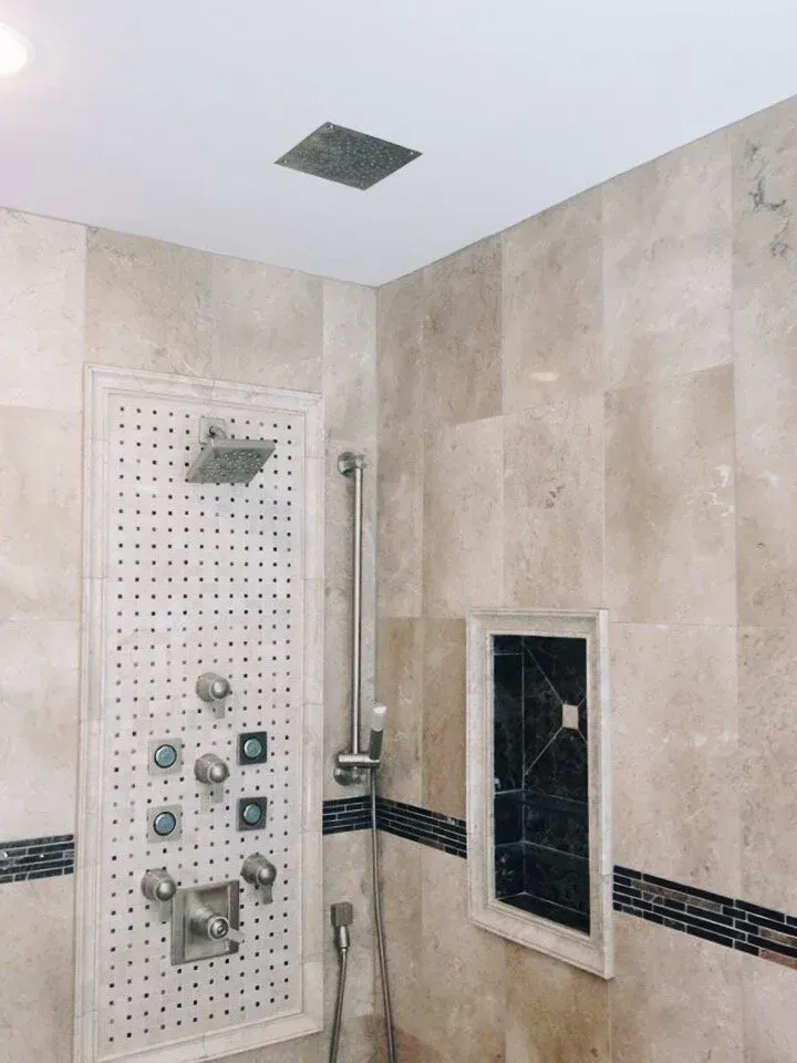Shower with beige tiled walls, multiple showerheads, and built-in shelf with decorative mosaic.