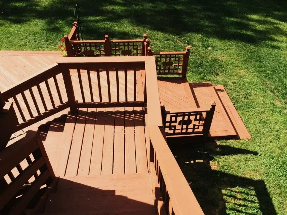 Wooden deck with railings, painted in reddish-brown, outdoors on green grass.