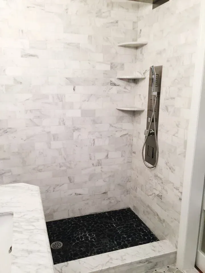 Shower with white marble walls, black tiled floor, and three built-in shelves.
