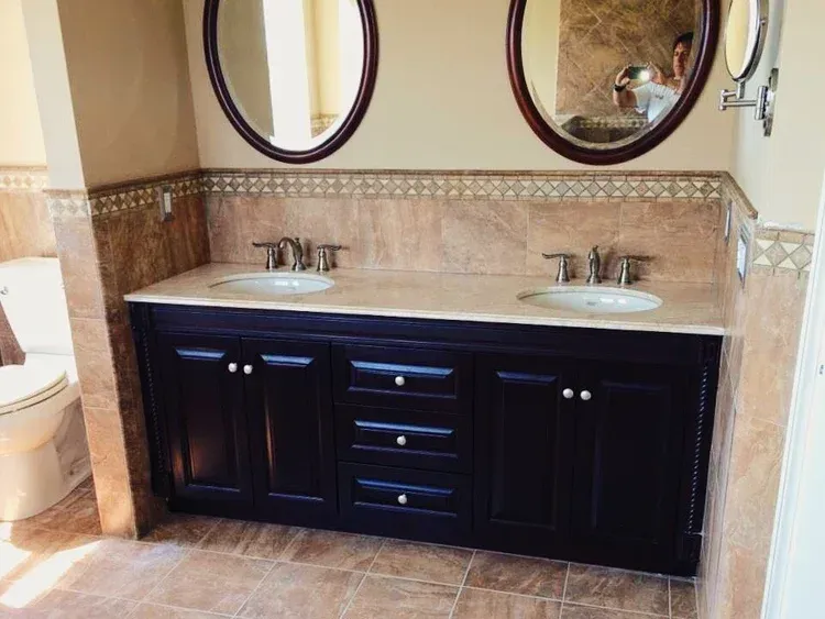 Bathroom vanity with two sinks, dark cabinets, oval mirrors, and tile.