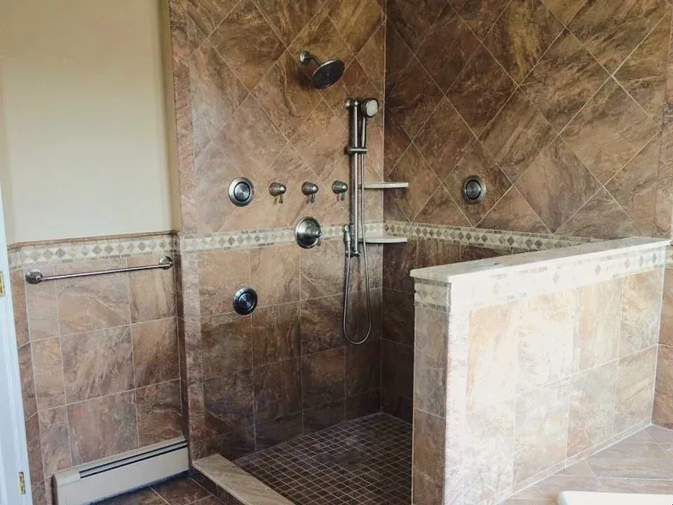 Spacious tiled shower with multiple showerheads and fixtures in a brown and tan bathroom.