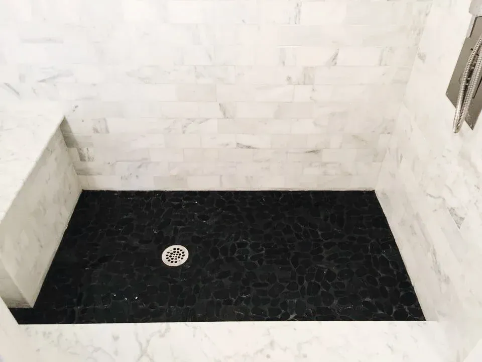 Black tile shower floor with white marble walls and a built-in seat.