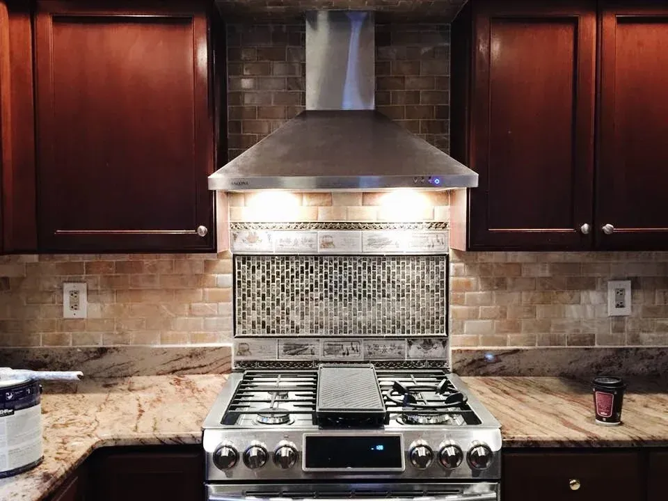Kitchen with stainless steel range and hood, brown cabinets, and a mosaic tile backsplash.