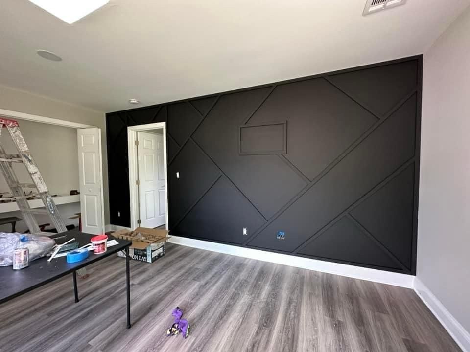 Black accent wall with geometric wood paneling, white trim, and gray flooring in a room.
