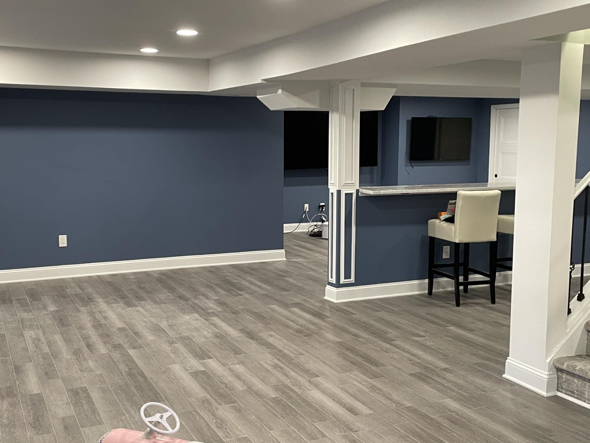 Finished basement with blue walls, gray flooring, white trim, and a bar area.