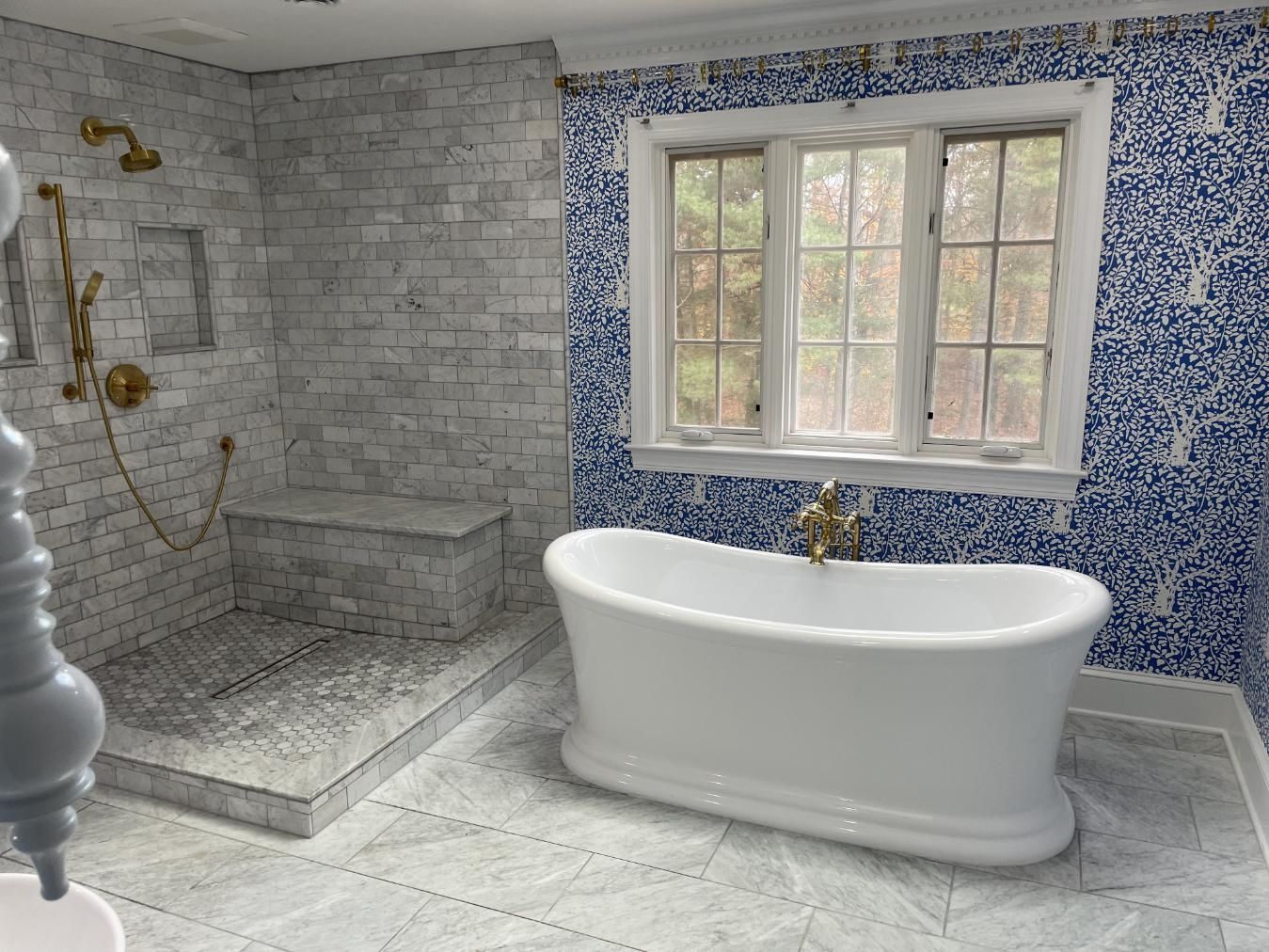 Bathroom with white tub, blue mosaic wall, and gray tile shower. Window in background.