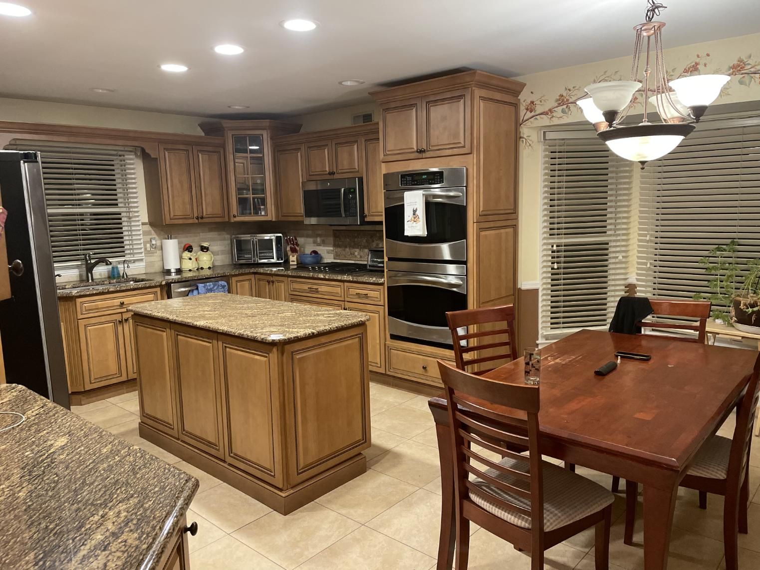 Kitchen with light brown cabinets, granite countertops, island, oven, microwave, and dining table.