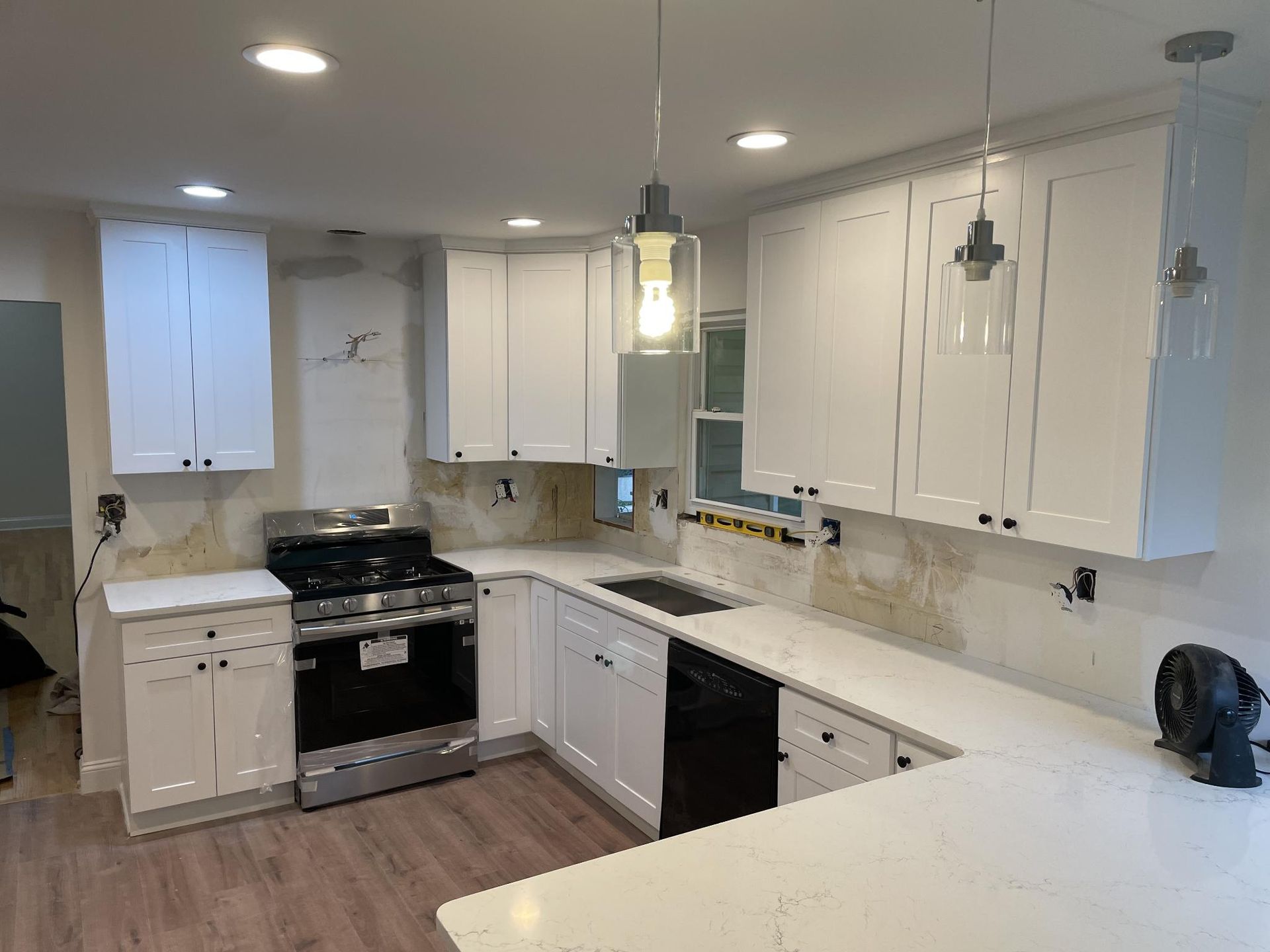 White kitchen cabinets, countertop, and appliances in a renovated kitchen with two pendant lights.