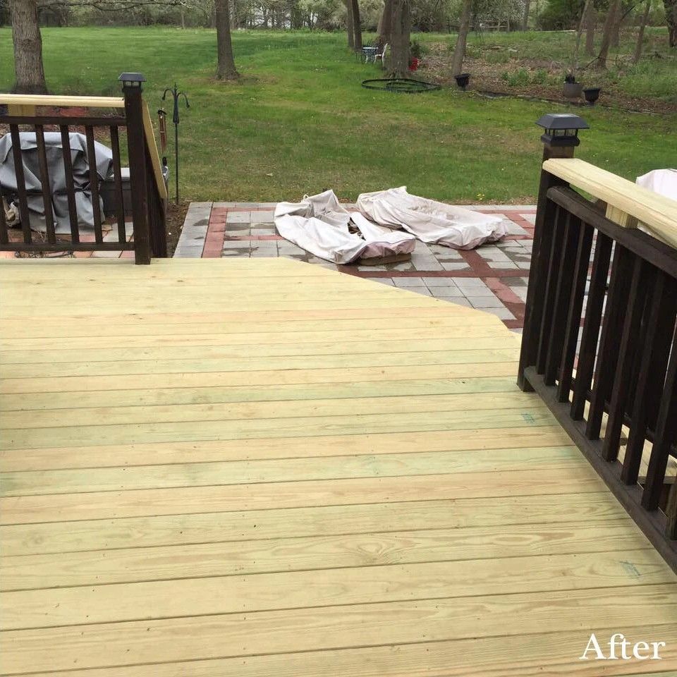 Newly stained wooden deck with dark railing and brick patio. Backyard setting.