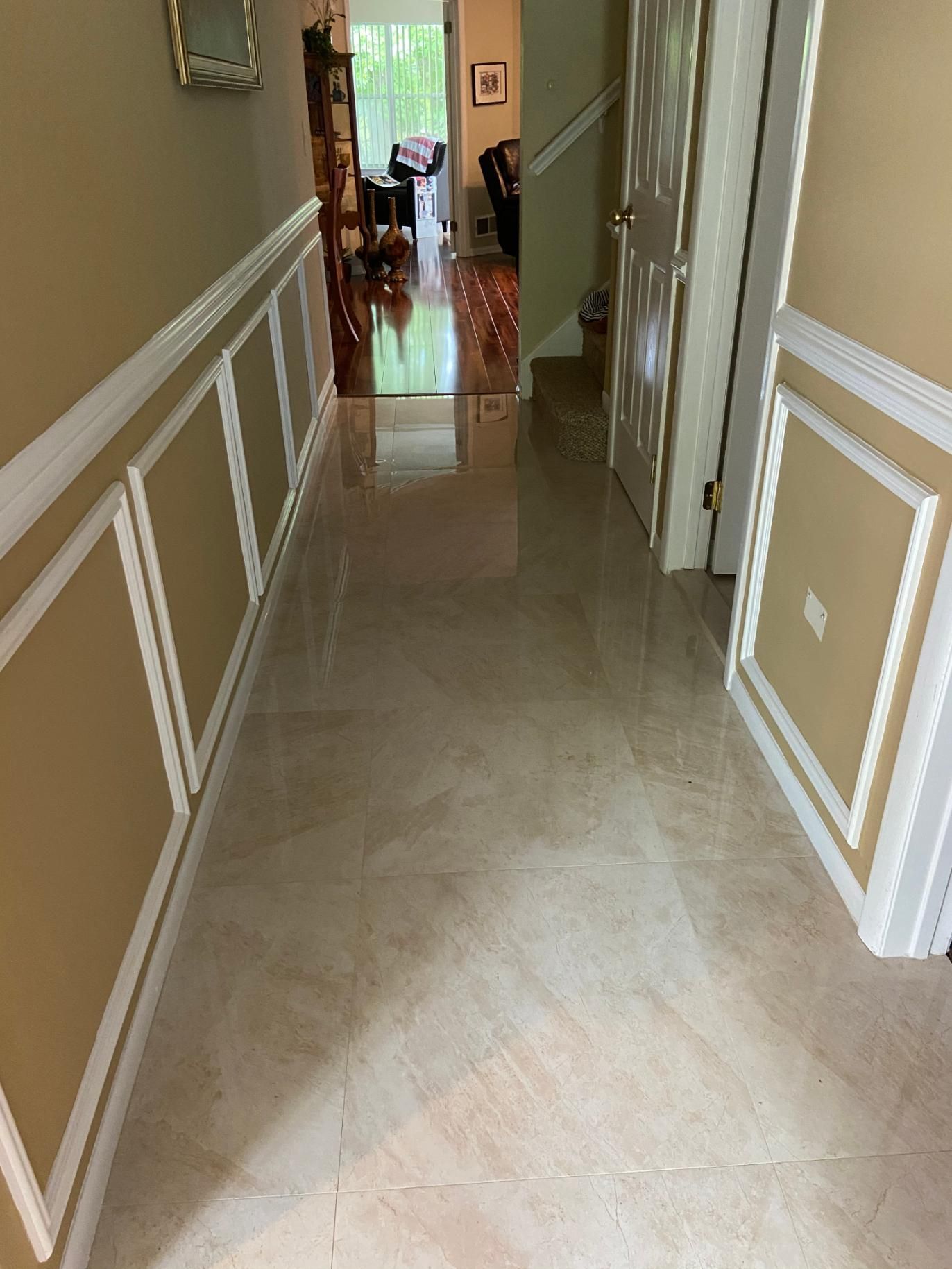 Hallway with tan tile flooring, cream-colored wainscoting, and a closed white door.