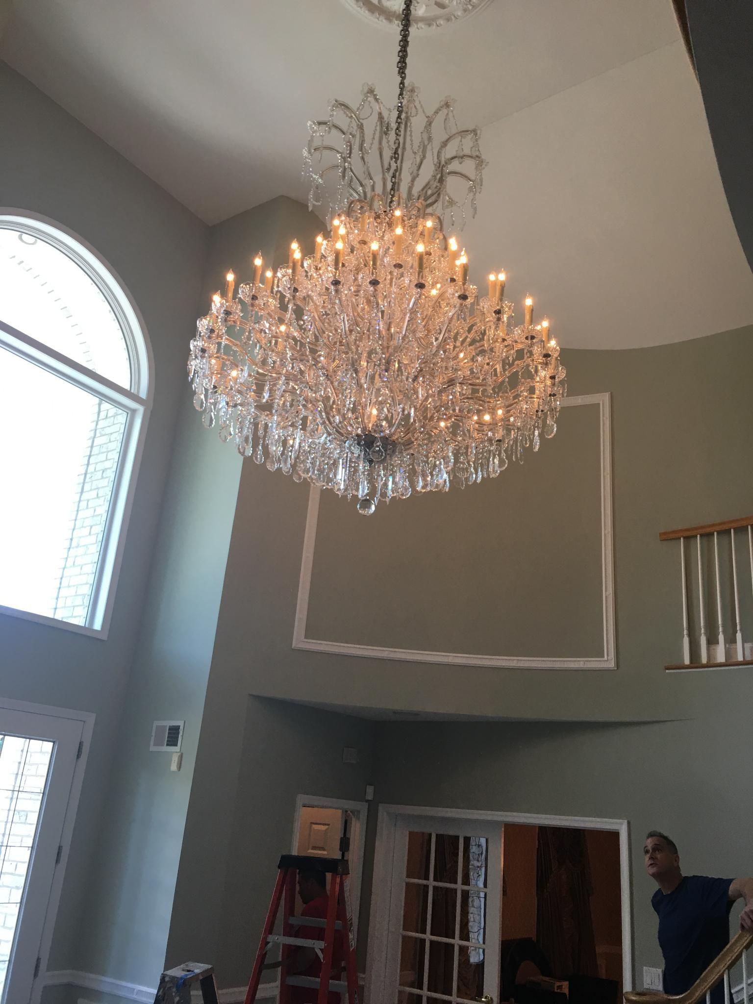 Large, ornate crystal chandelier hangs in a high-ceilinged room with a man standing near a door.