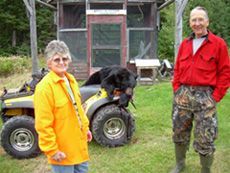 A man and a woman are standing next to a bear on a four wheeler.