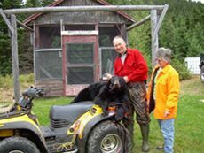 A man and a woman are standing next to a four wheeler with a bear on it.