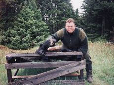 A man is standing next to a black bear behind a wooden fence.