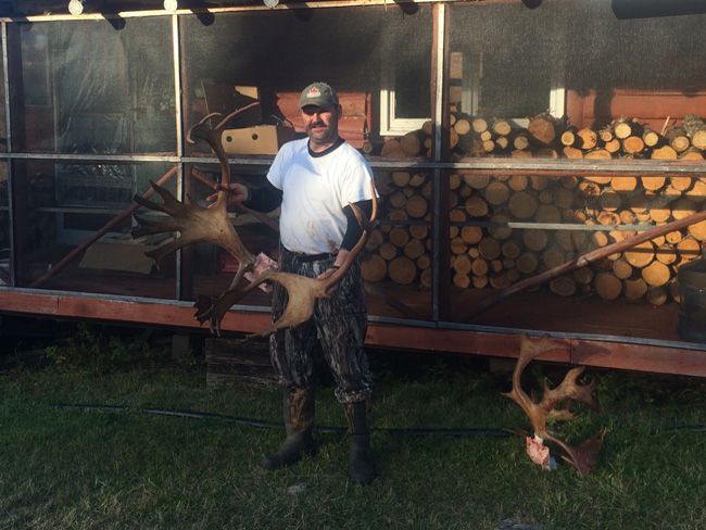 A man in a white shirt is holding a large deer antlers