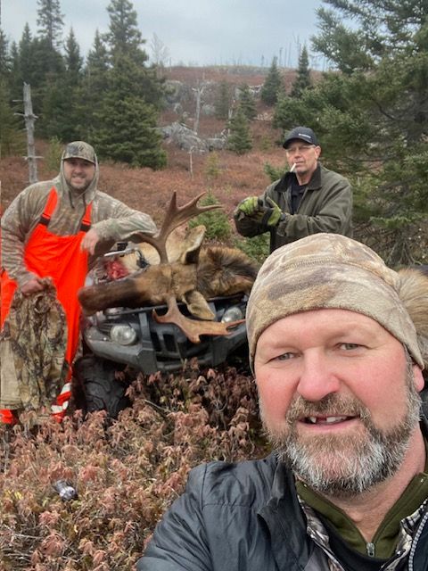 Three men are standing next to a moose on a four wheeler.