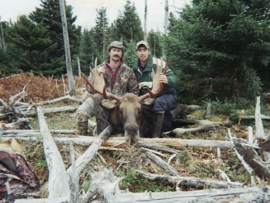 Two men are posing for a picture with a moose in the woods.