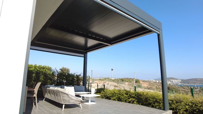 Patio moderno con pergola scura, sedie a sdraio bianche e vista sull'oceano.