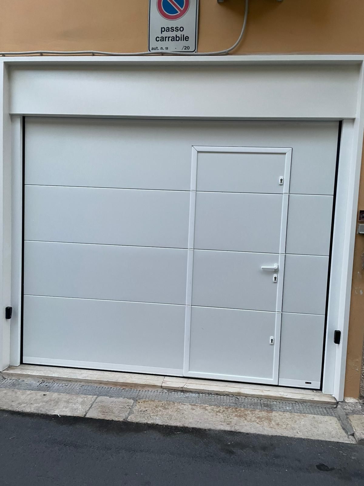 Porta da garage grigia chiusa con una piccola porta laterale su un edificio che si affaccia sulla strada.