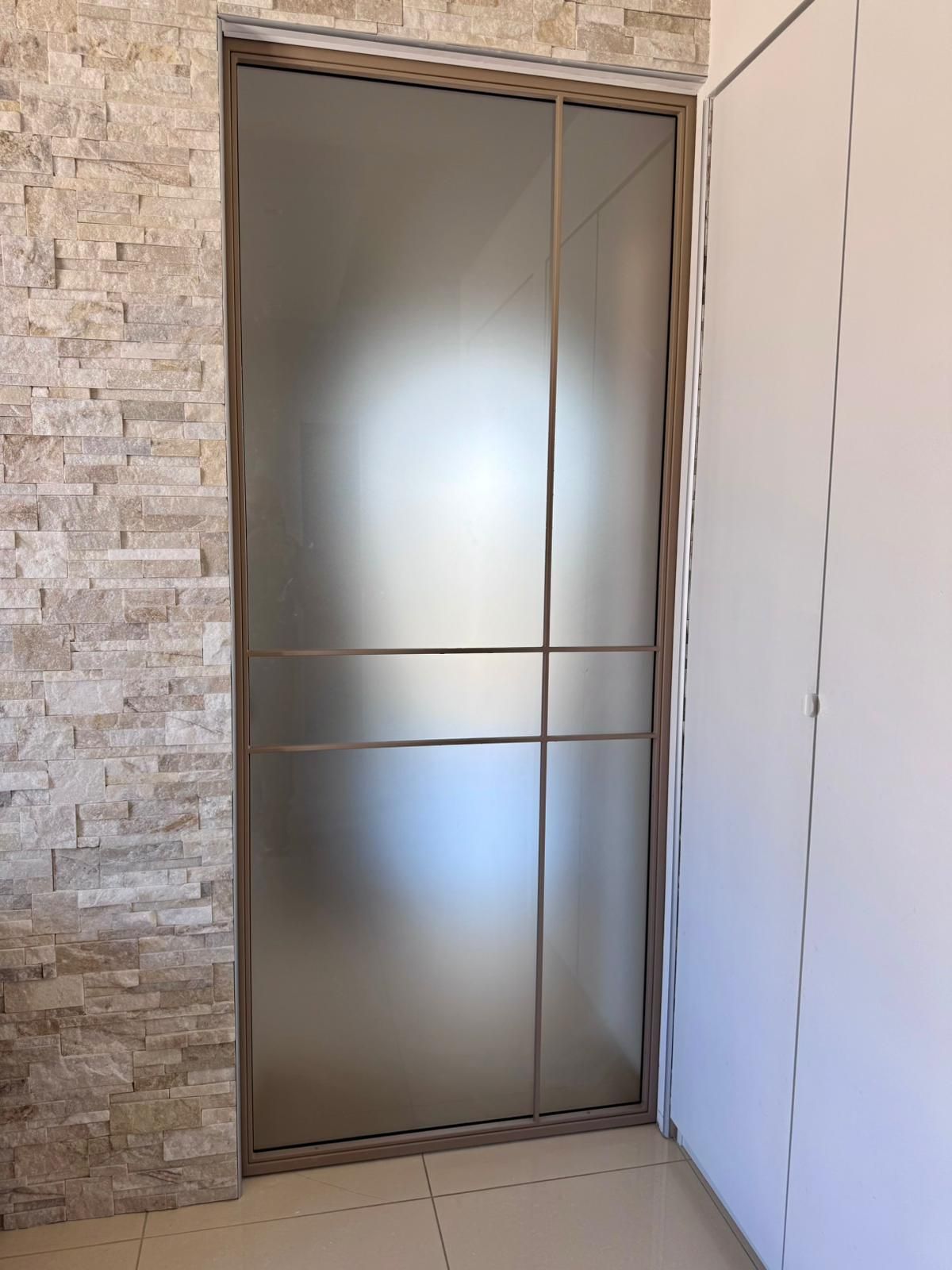 Porta scorrevole chiusa in vetro smerigliato in un corridoio interno con pareti in pietra.